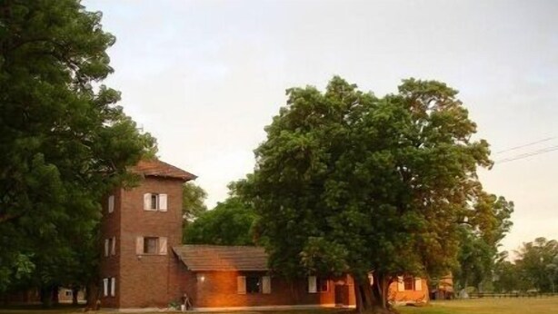 Un edificio de ladrillo de dos pisos con una estructura tipo torre, rodeado de árboles y un área verde.