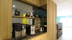 Eine Kaffeestation mit Kaffeemaschine und Wasserspender, ein Regal mit Dekorationsobjekten sowie ein Tresen mit Mülleimer.