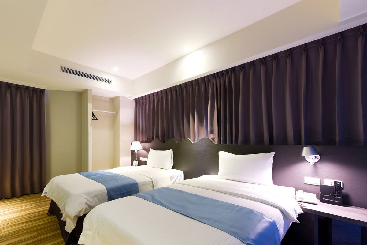 Ein Hotelzimmer mit zwei Betten, einem Schreibtisch mit Lampe, einem Telefon und einer Minibar.
