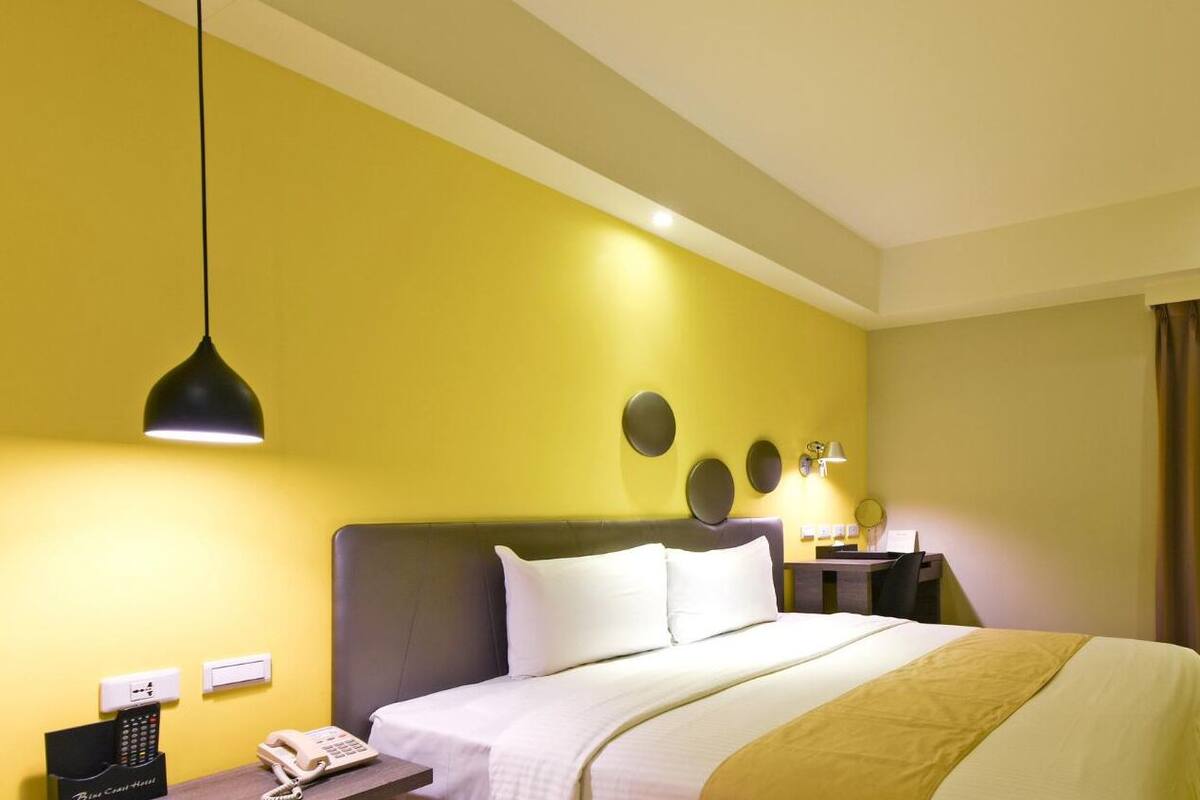 Ein Hotelzimmer mit einem Bett, Nachttischen, einem Schreibtisch, einem Telefon, einem Fernseher und einem Vorhang.