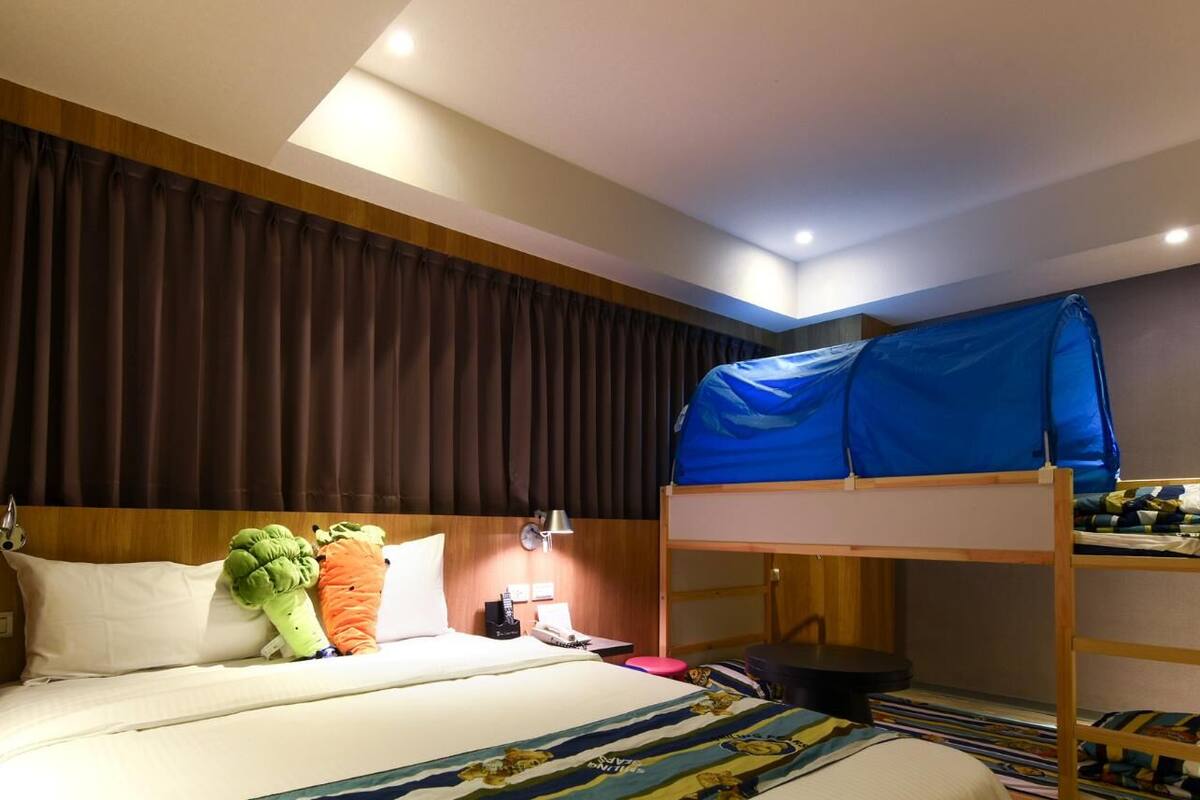 Ein Hotelzimmer mit Etagenbett, einem Einzelbett, einem hölzernen Kopfteil, einer Wandlampe und einer Deckenleuchte.