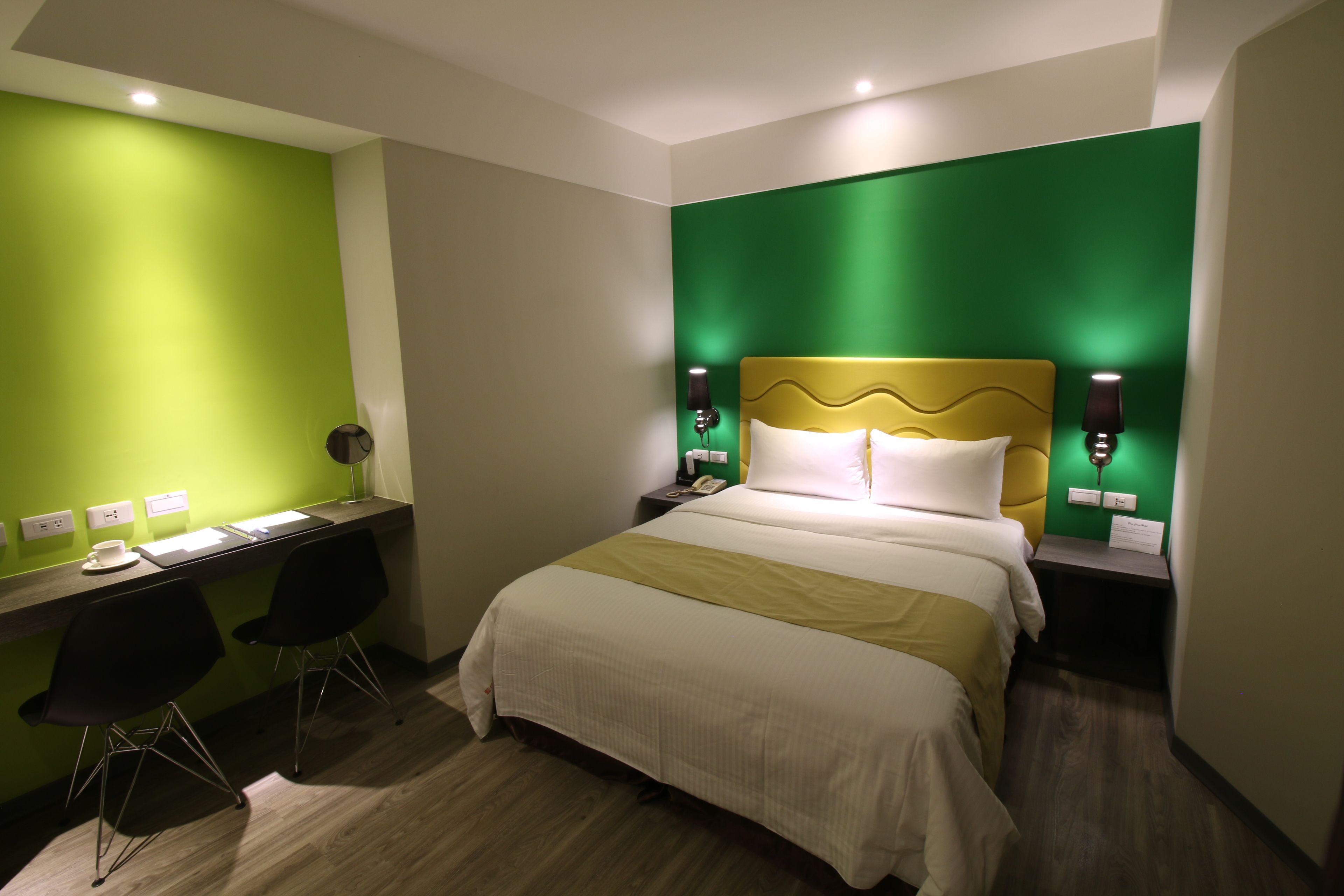 Una camera d'albergo con un letto, una scrivania, due sedie e una parete verde decorativa.