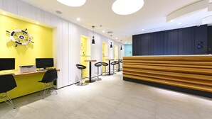 Ein moderner Empfangsbereich mit Holzbüro, mehreren Barhocker und einer gelben Wand mit Schiffswellen-Dekoration.