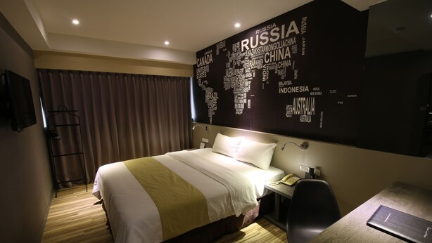 Ein Hotelzimmer mit einem großen Bett, einem Schreibtisch, einem Stuhl, einem Telefon und einer Wand mit einer Weltkarte.