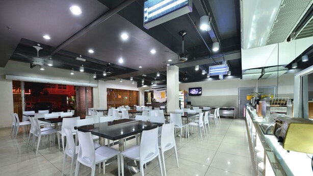 Eine großzügige Cafeteria mit weißen Tischen und Stühlen, einem Fernseher und einer Speisenauslage.
