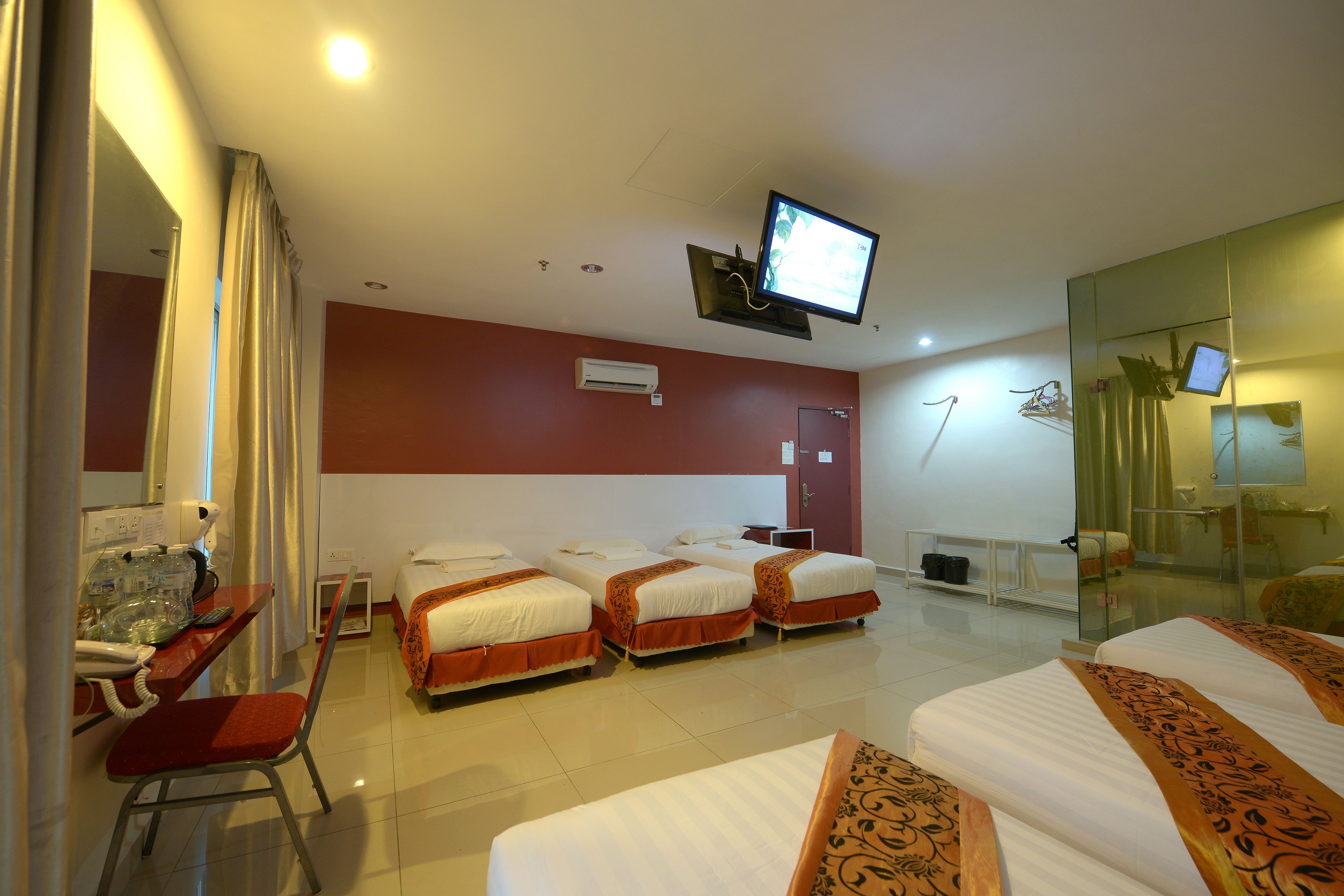 A hotel room with four beds, a desk with a chair, a television, and a glass partition.