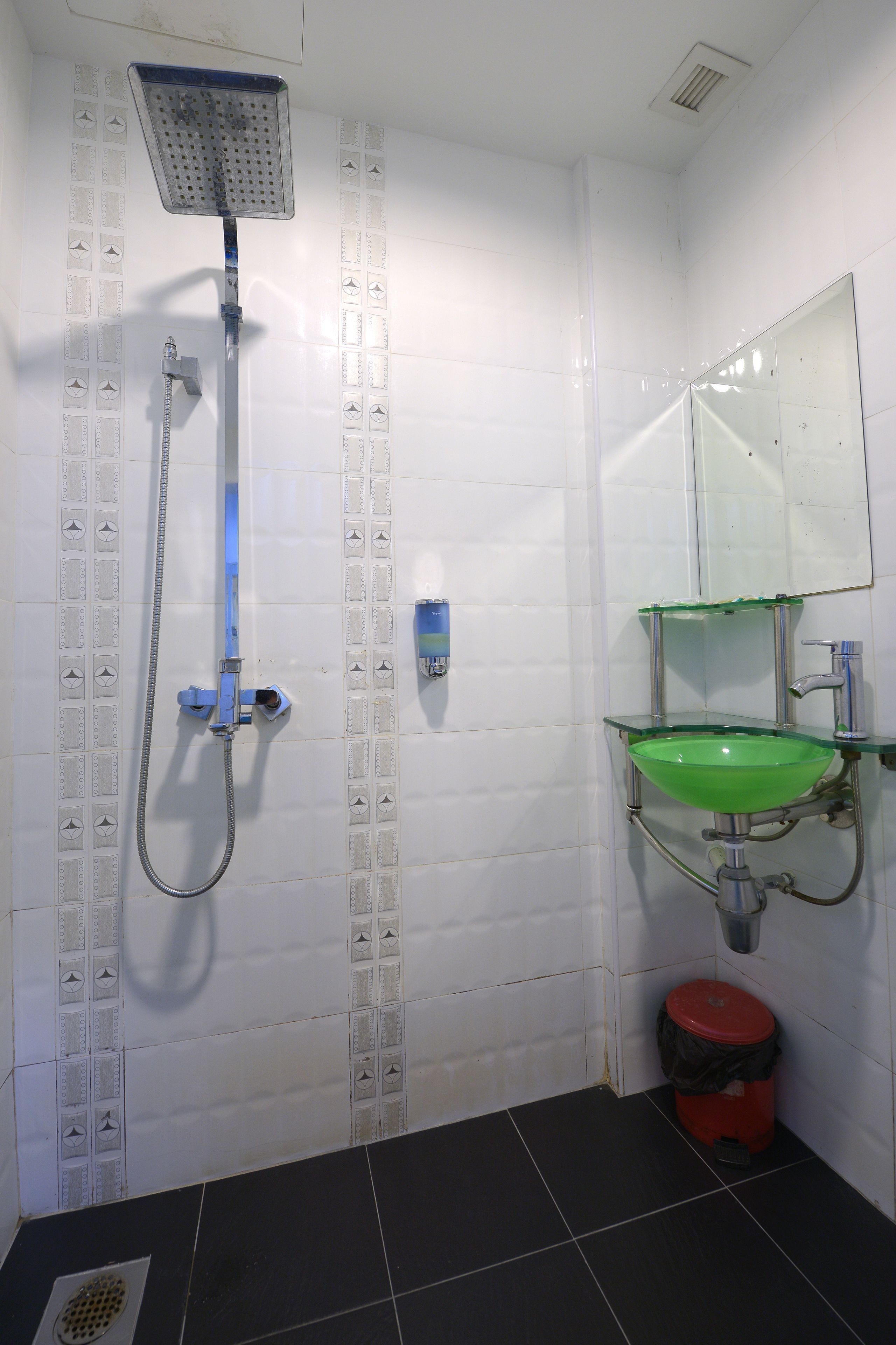 A bathroom with a shower, a green sink, and a red trash bin.