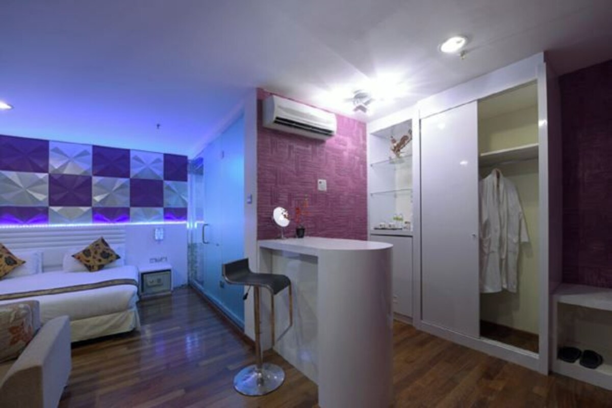 Habitació d'hotel moderna amb un llit, una petita zona de bar, un tocador amb mirall, un armari i una calaixera per sabates.