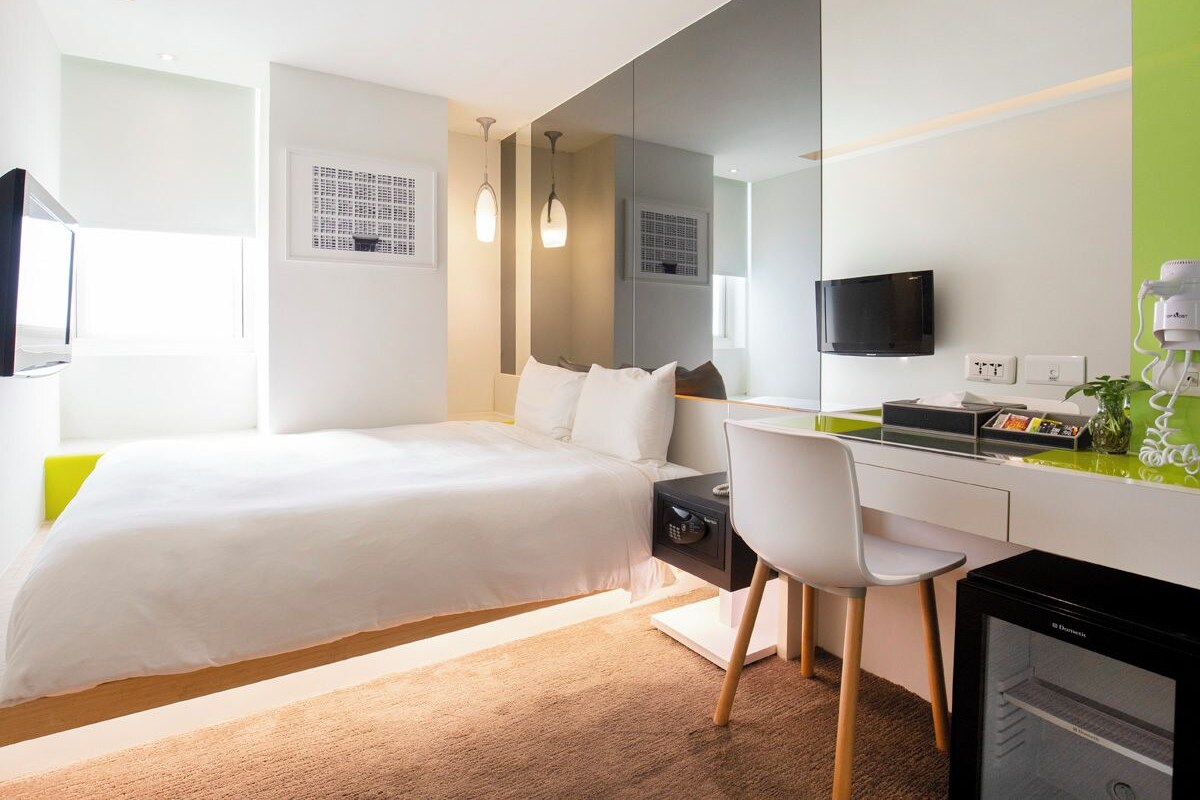 Una habitación de hotel moderna con cama, escritorio, silla y un espejo grande.
