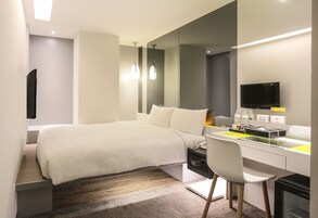 Una habitación de hotel moderna con cama, escritorio, silla y televisor de pantalla plana.