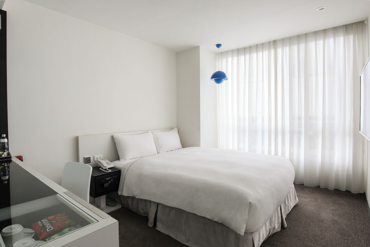 Una habitación de hotel con una cama, mesita de noche y un escritorio con silla.