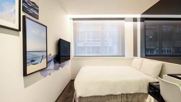 A modern hotel room with a large bed, a flat-screen TV, and a window with a city view.