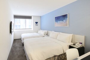 Een hotelkamer met twee bedden, een klein bureau met telefoon, een raam en een schilderij aan de muur.