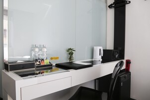 Habitación de hotel moderna con un escritorio blanco, una silla negra, una cafetera y una pequeña planta en maceta.