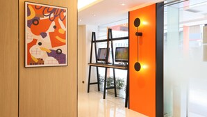 A modern interior with a wooden panel wall, a colorful abstract painting, and a glass partition with two monitors.