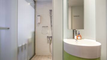 A modern bathroom with a glass shower enclosure, a white sink with a green base, and a mirror above the sink.