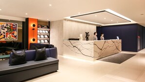 A modern reception area with a marble reception desk, a sofa with black cushions, and a colorful abstract painting on the wall.
