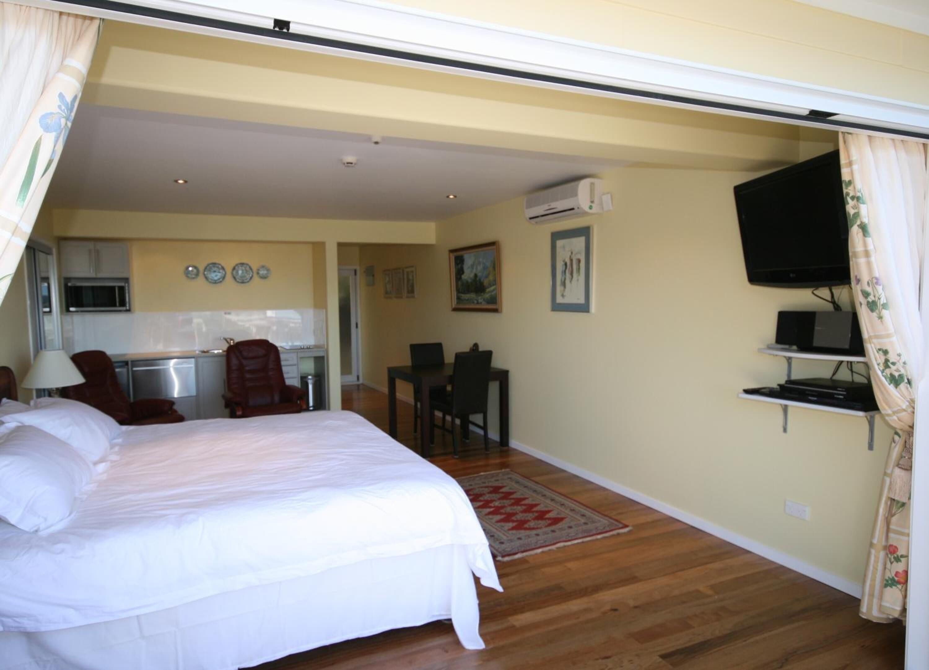Een slaapkamer met een bed, een bureau, een stoel, een televisie en een airconditioning.