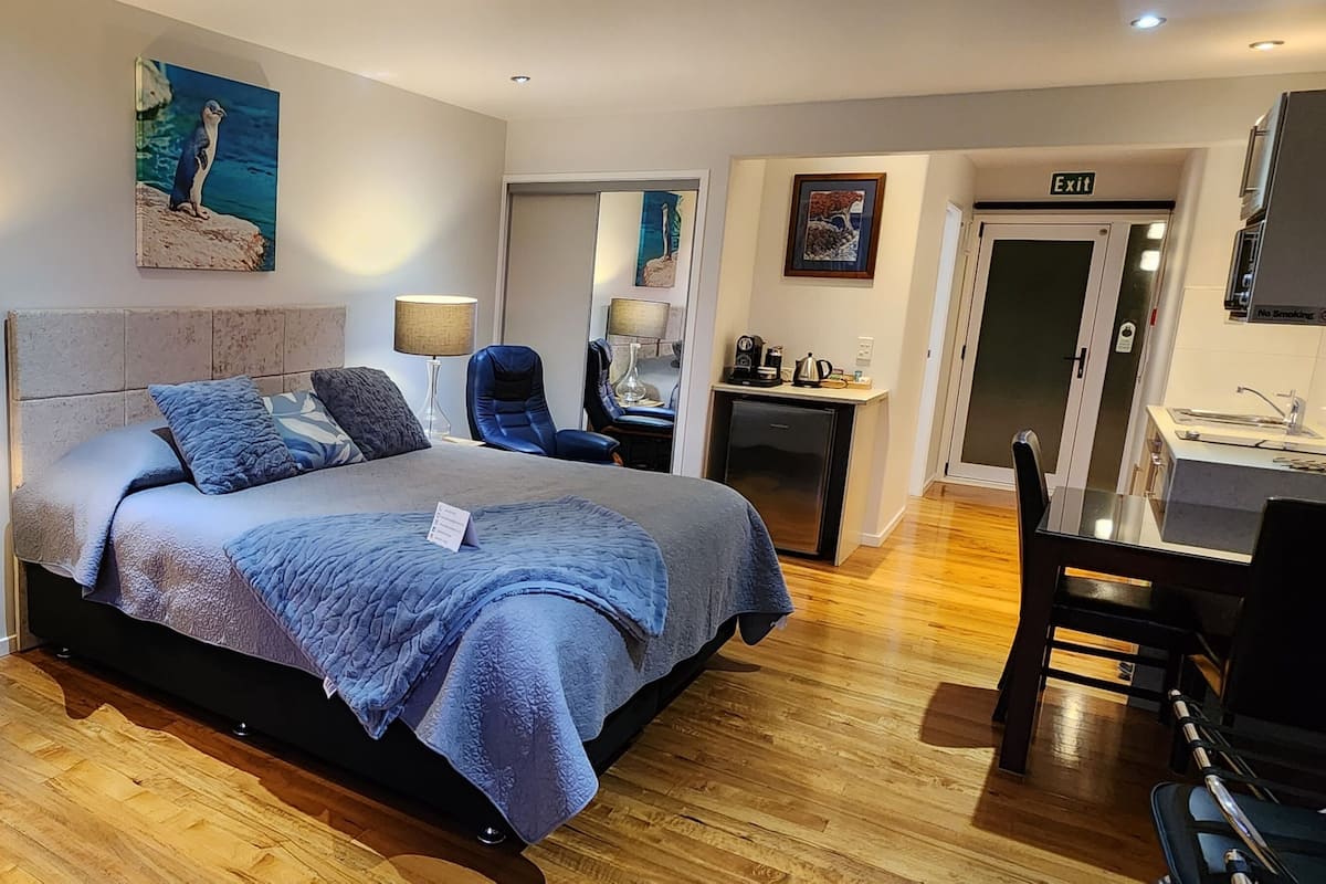 A modern hotel room with a bed, a desk, a chair, a lamp, and a painting on the wall.