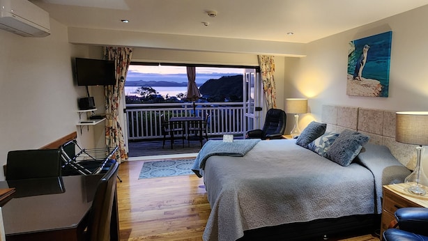 Habitación de hotel con cama, escritorio, silla, televisor y balcón con vistas al mar.