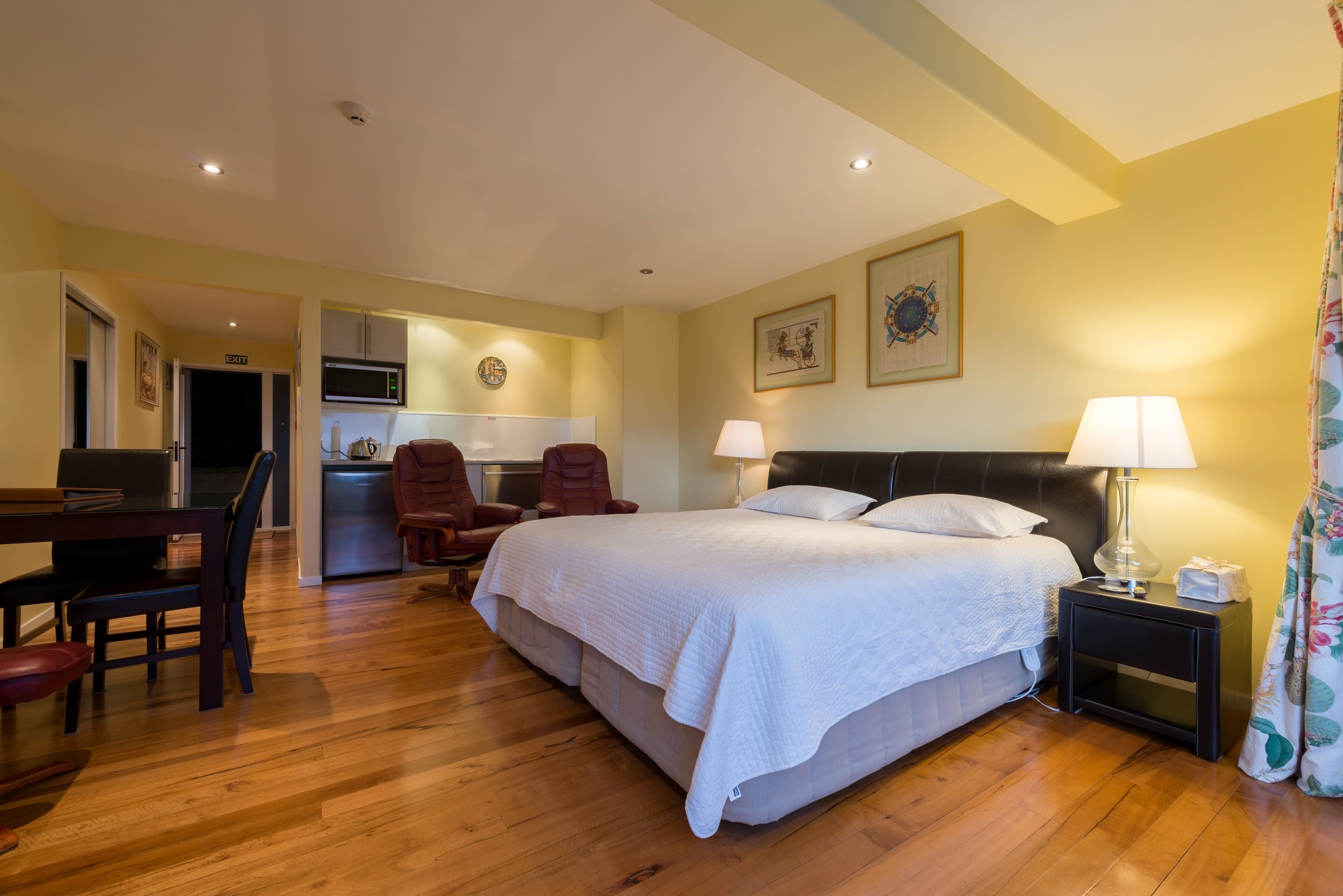 Een hotelkamer met een bed, nachtkastje, lamp en uitzicht op de keuken.