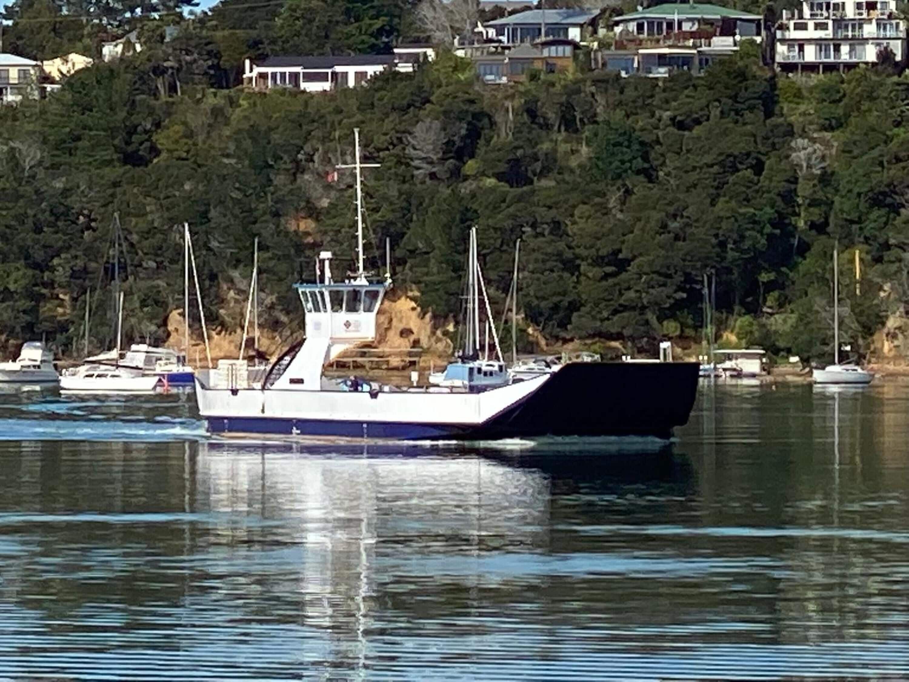 A large boat docked at a harbor with a forested hillside in the background.