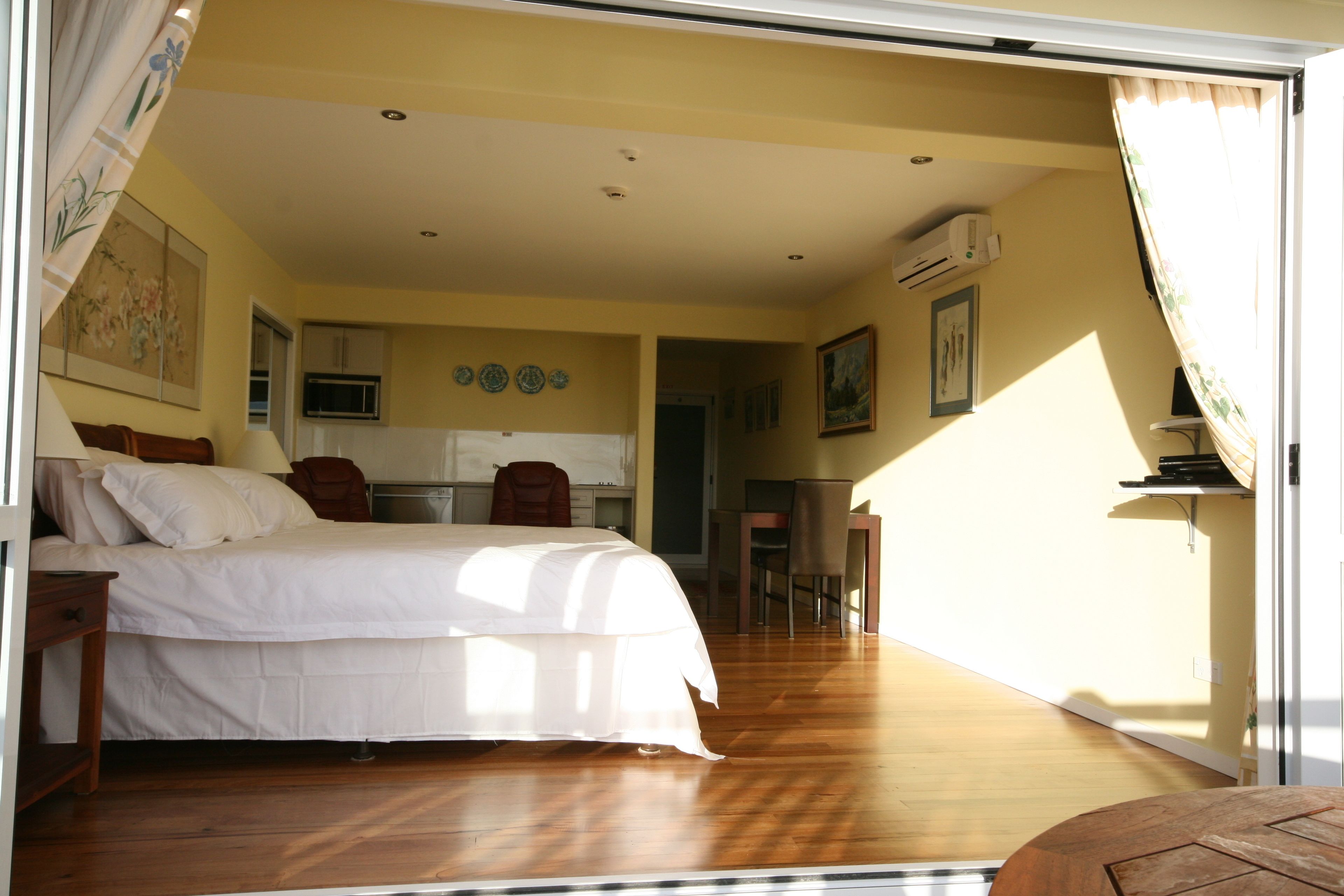 Quarto com uma cama grande, uma mesa de escritório e uma cadeira. Há uma área de cozinha com armários e um micro-ondas.