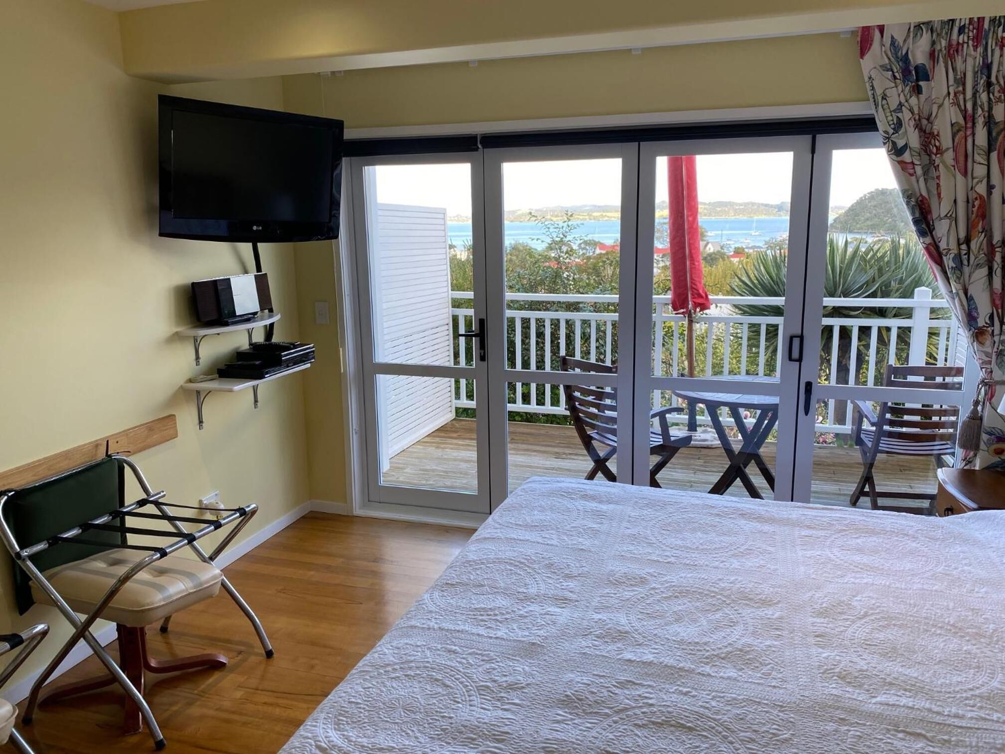 Une chambre avec un lit, un téléviseur fixé au mur, un balcon avec une table et des chaises, et une vue sur la mer.