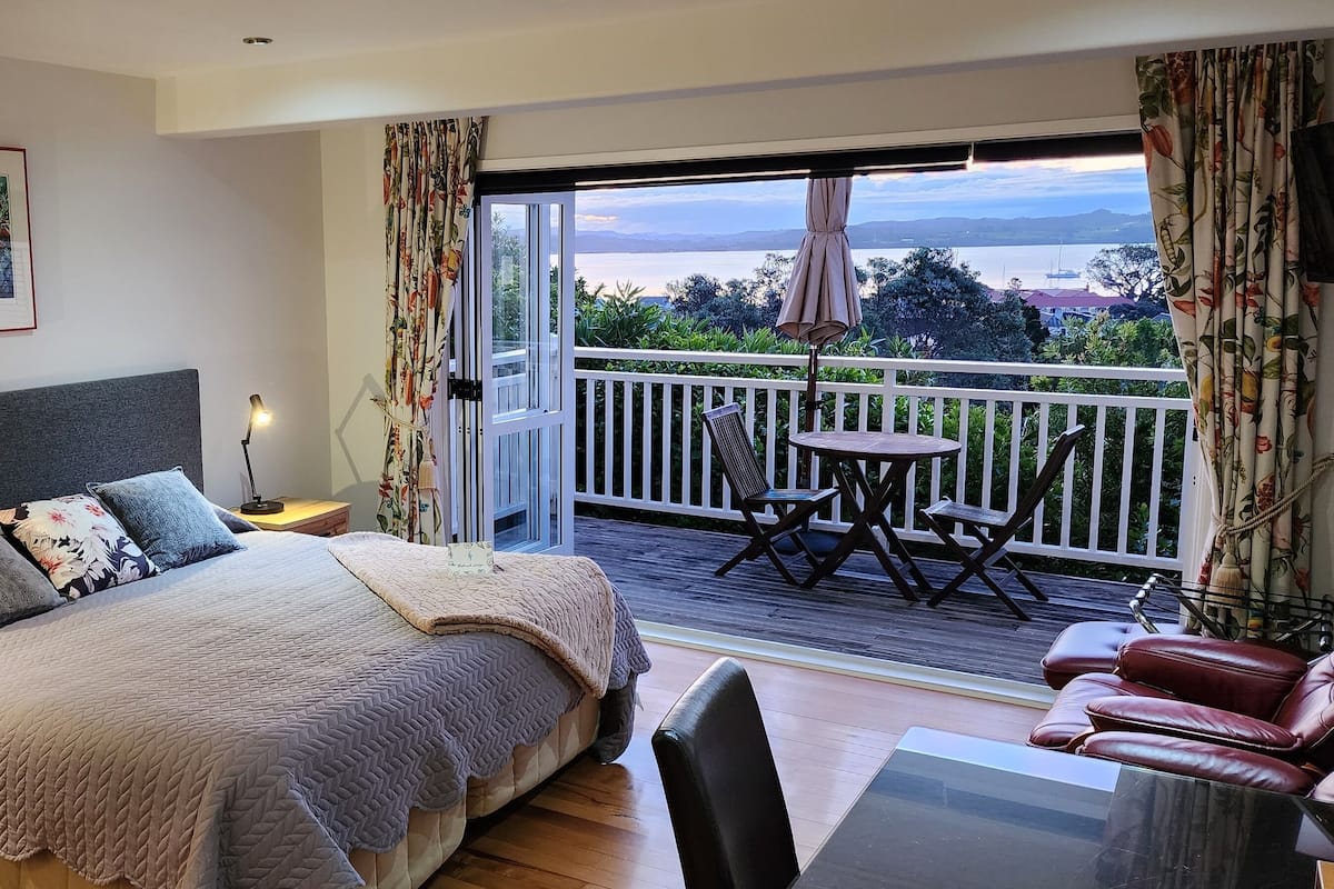 A bedroom with a bed, bedside table, lamp, and a balcony with a table and chairs.