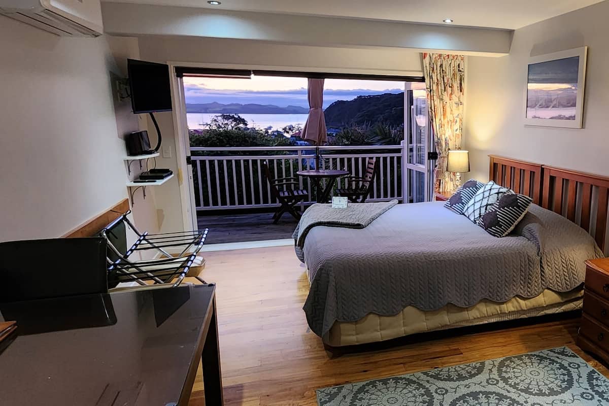 A bedroom with a bed, bedside table, lamp, and a view of the outdoors.