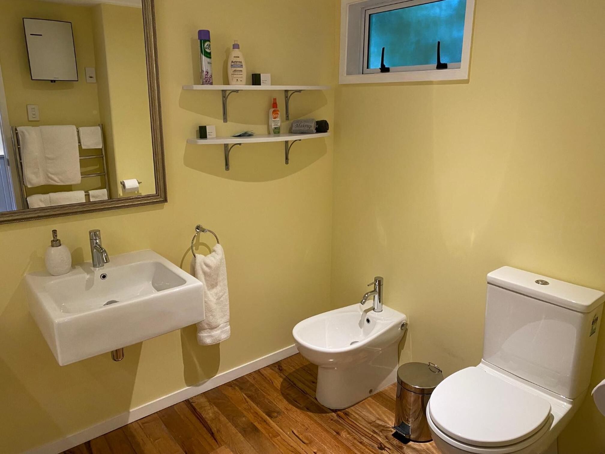 A bathroom with a sink, bidet, toilet, and shelves with toiletries.