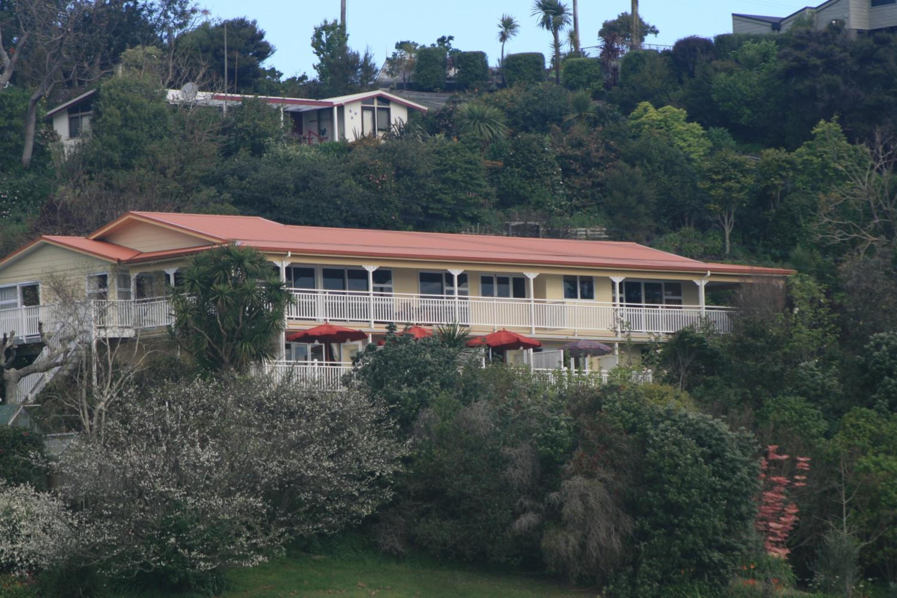 Un edificio de dos pisos con techo rojo, barandillas blancas en el balcón y sombrillas rojas.