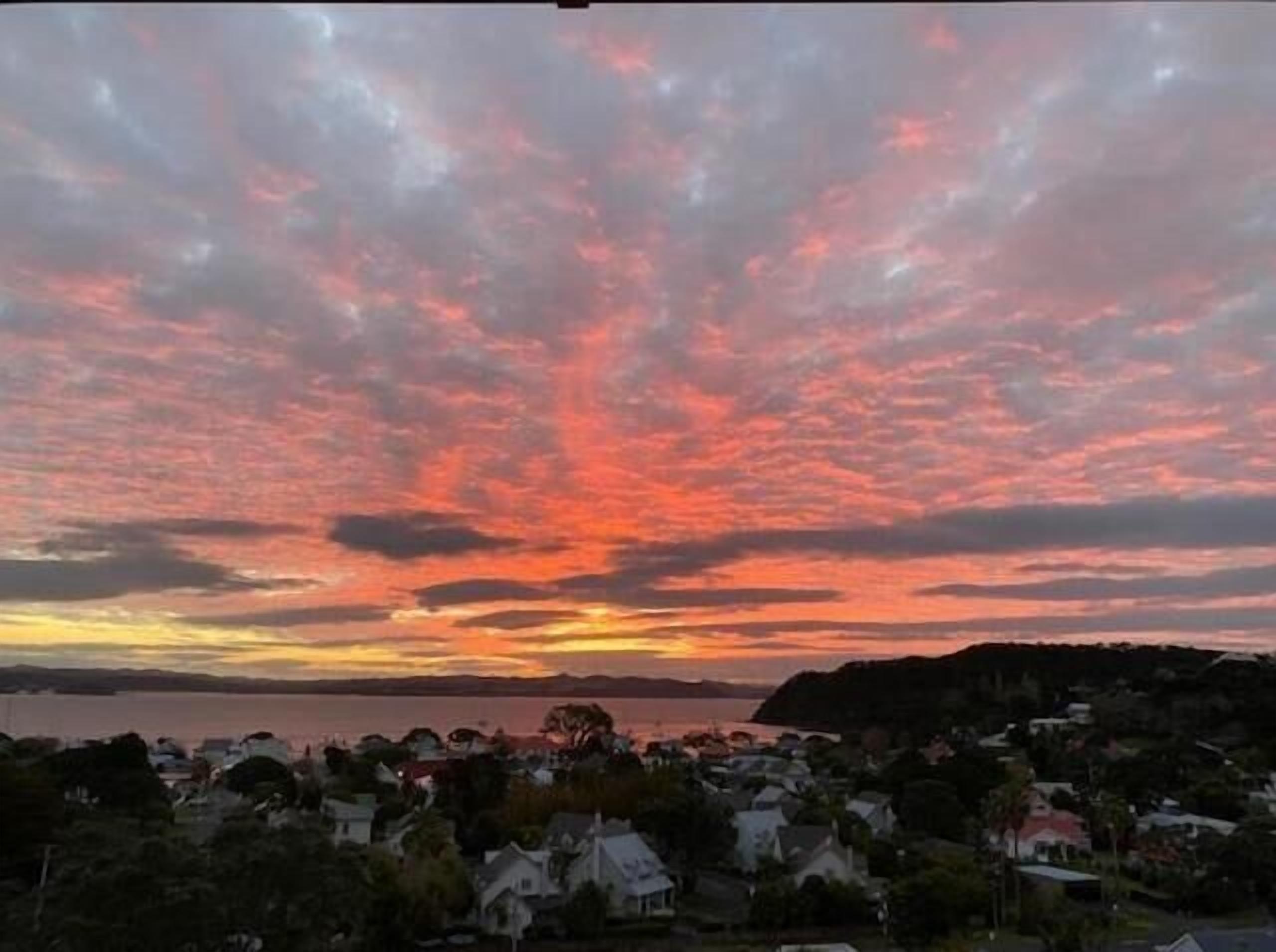 A coastal town at sunset with a view of the sea and hills in the background.
