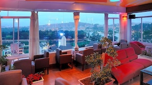 A spacious living area with a large window offering a city view, comfortable seating, and a modern ceiling design. - Thi Thao Gardenia Hotel (Xuan Huong - Da Lat)