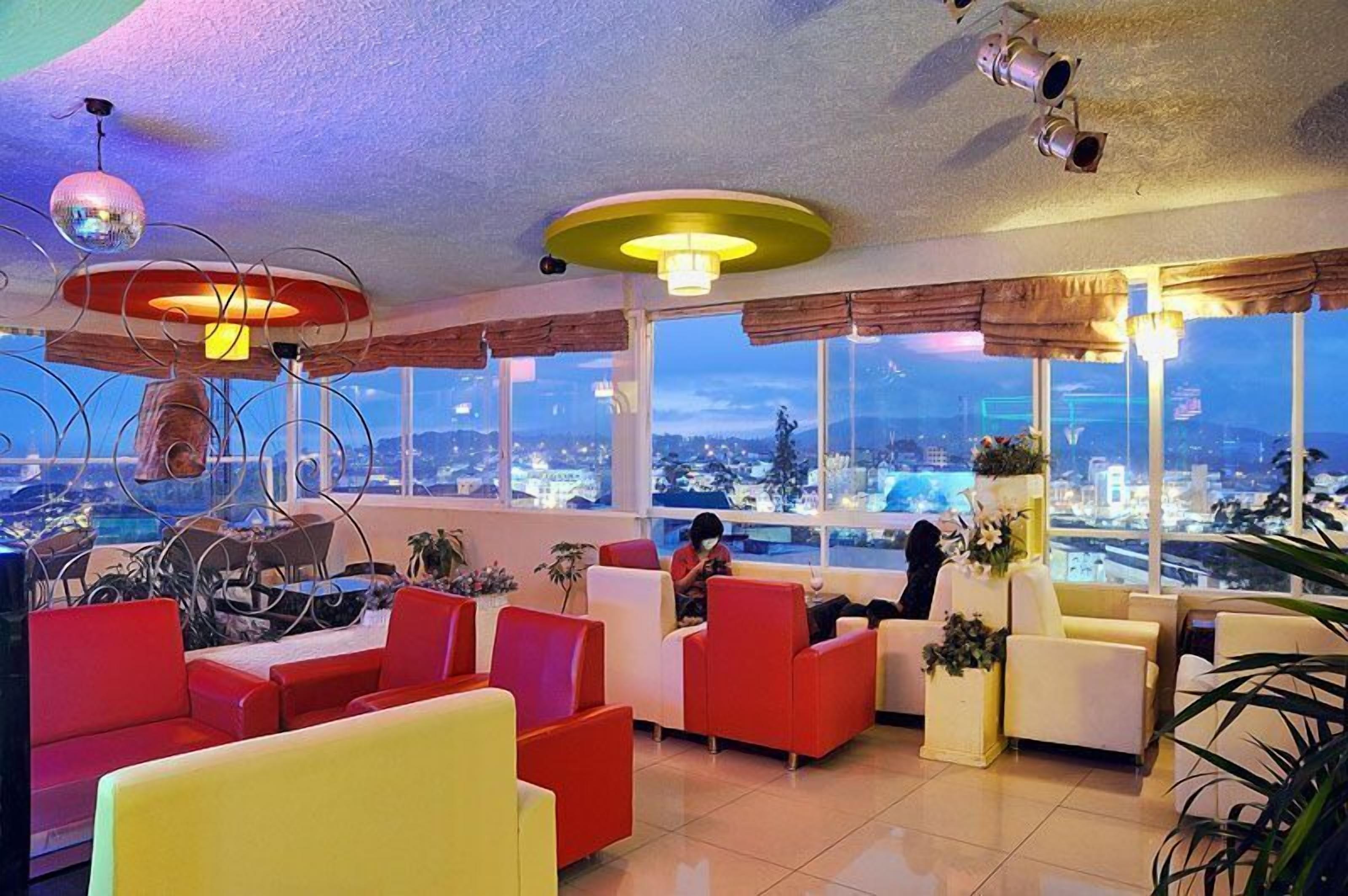 Un salón moderno con sillones rojos y blancos, amplias ventanas con vistas a la ciudad e iluminación de techo original.
