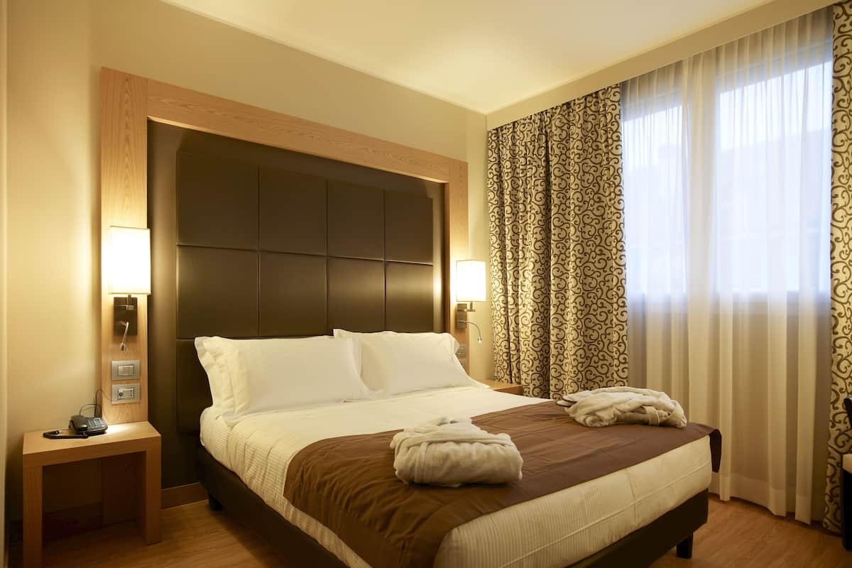 A hotel room with a large bed, two bedside tables, a wall-mounted lamp, and patterned curtains.