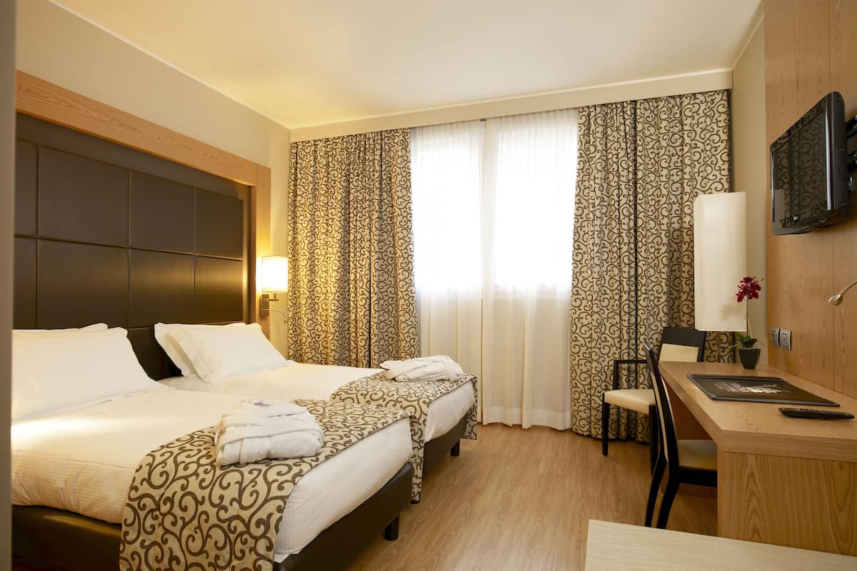 A hotel room with two beds, a desk, a chair, a TV, and curtains.