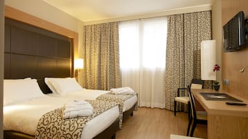 A hotel room with two beds, a desk, a chair, a TV, and curtains.
