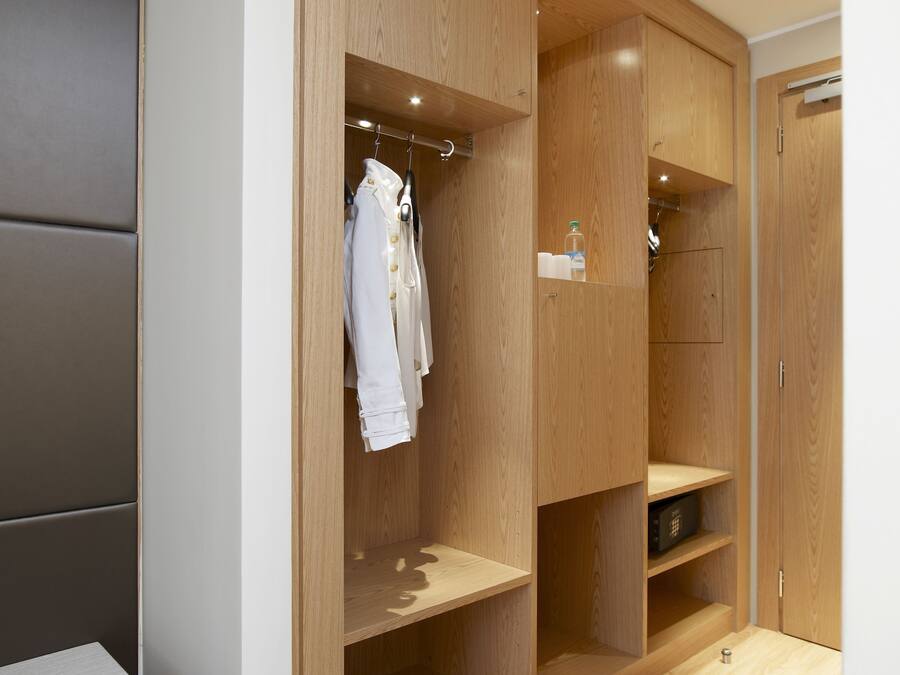 A walk-in closet with wooden shelving and hanging space, a bench, and a small shelf with toiletries.