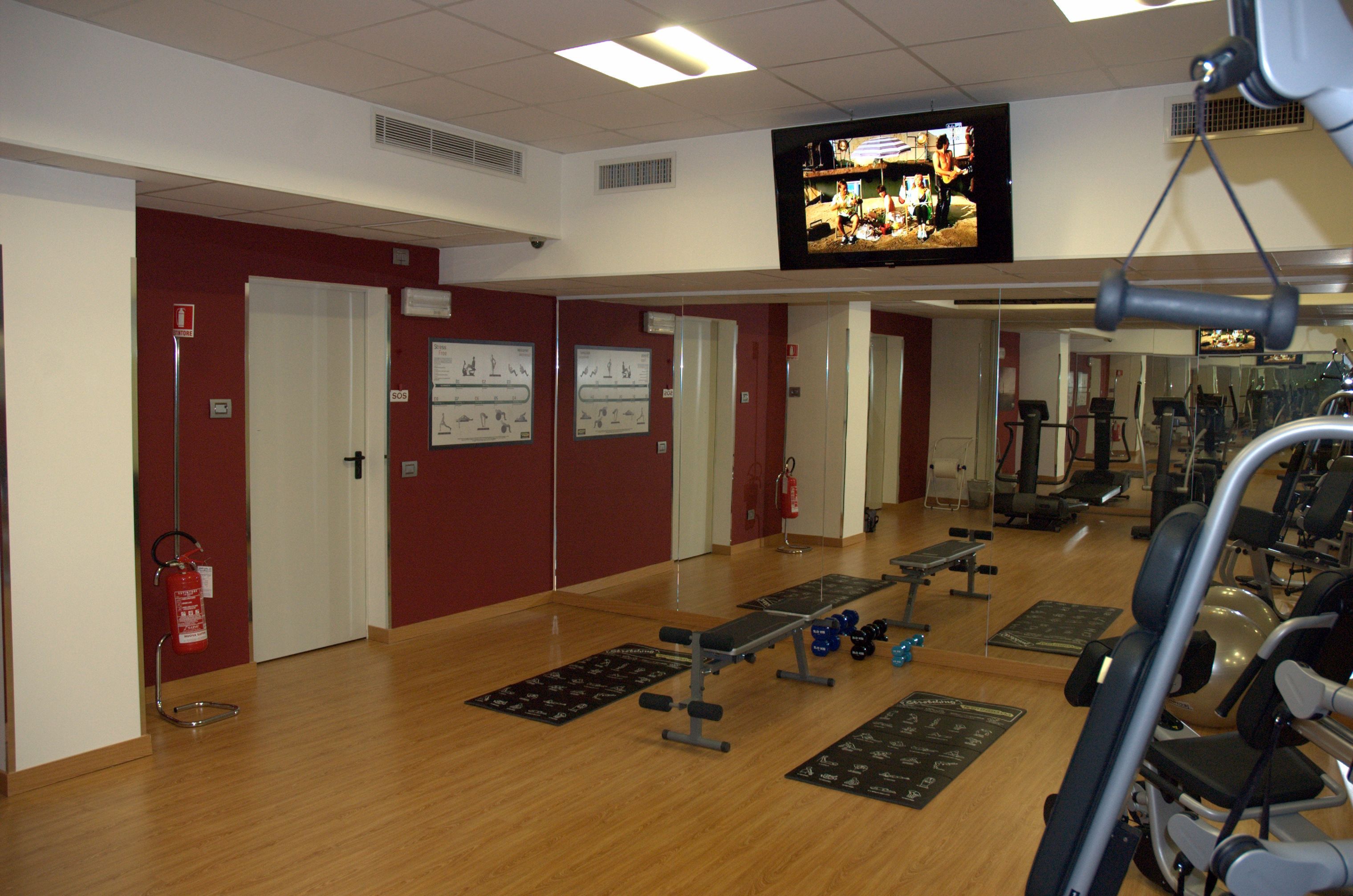 Un gimnasio con equipo de ejercicio, un televisor en la pared y un extintor.