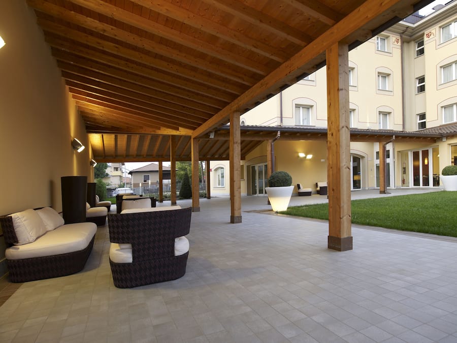 An outdoor covered seating area with wooden beams, a tiled floor, and a building in the background.