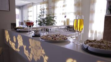 A buffet table with various food items and drinks, a decorative wall, and a large window with curtains.