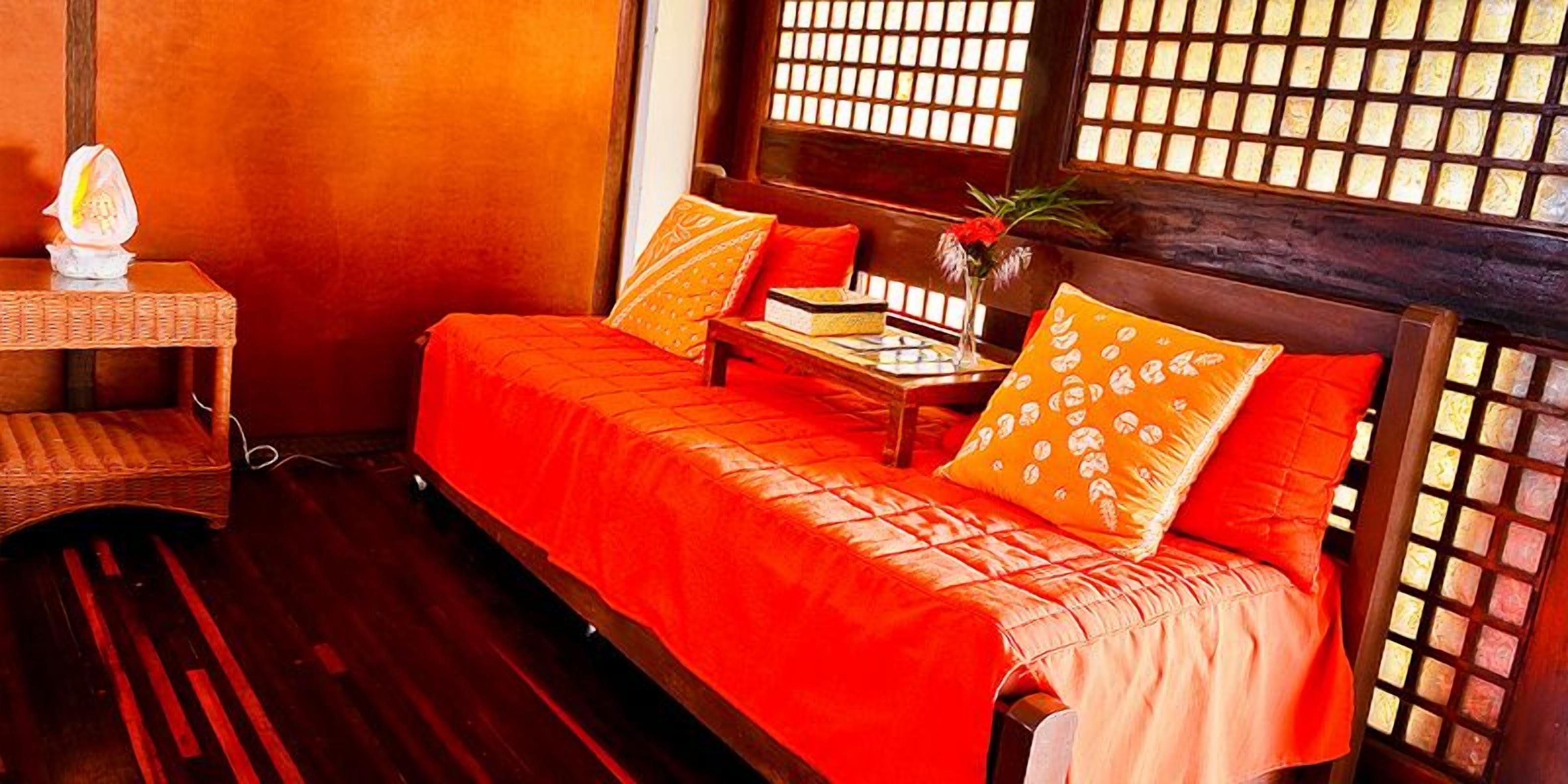 A room with a bed, a nightstand, a lamp, and a window with a wooden lattice.
