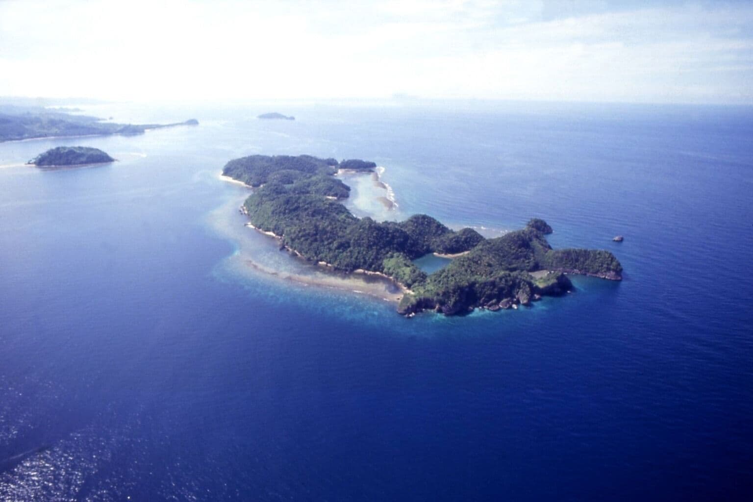 An aerial view of a chain of islands with clear blue waters and dense green vegetation.