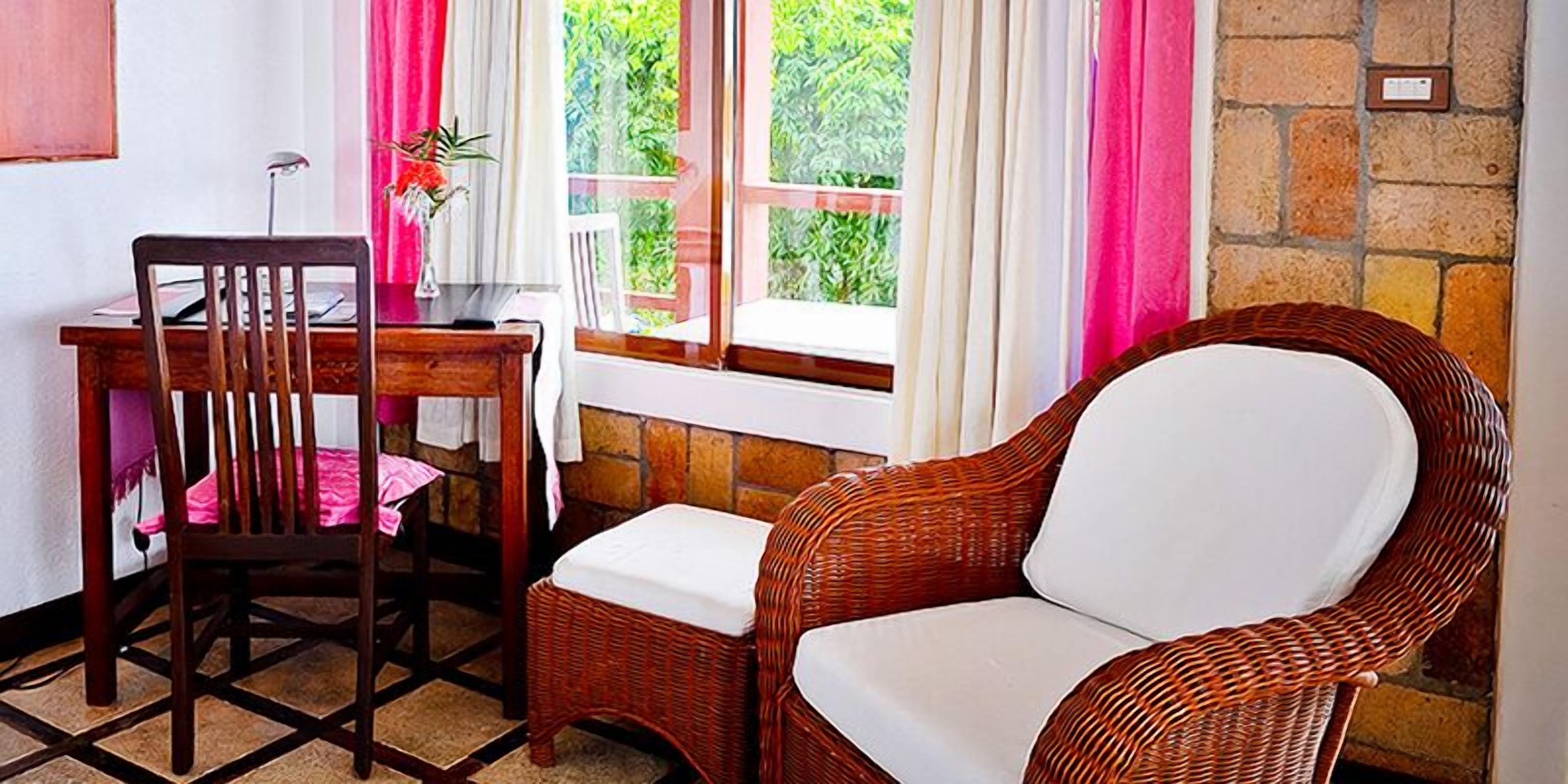 Una habitación con un escritorio de madera, una silla de mimbre y una ventana con cortinas.