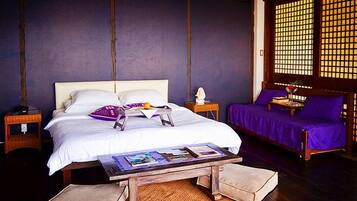 A bedroom with a bed, bedside tables, a reading table, and a purple sofa.