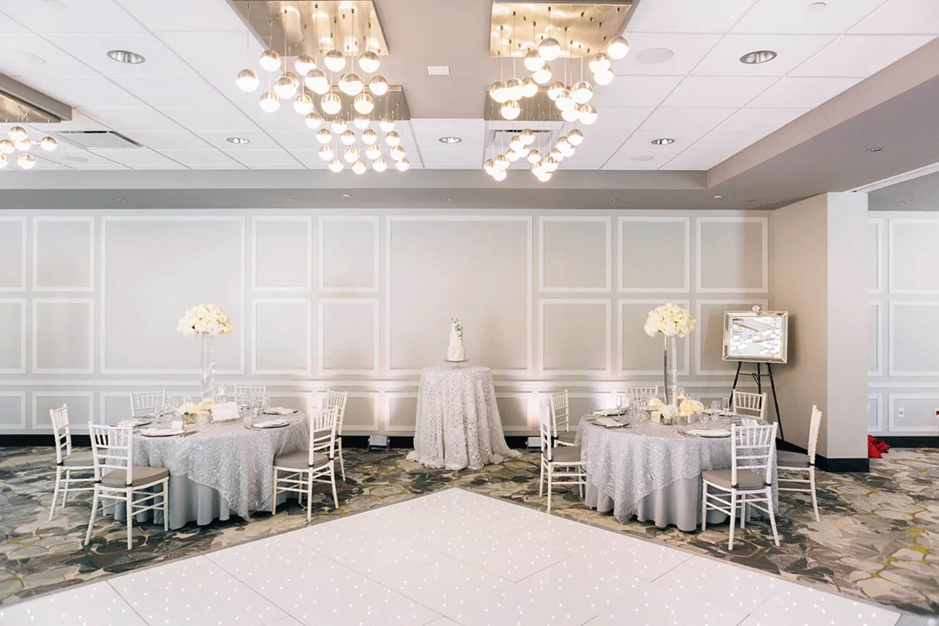 A banquet hall with round tables, white chairs, and floral centerpieces.