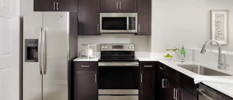 Una cocina moderna con electrodomésticos de acero inoxidable, armarios oscuros y encimera blanca.
