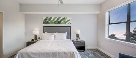 Una habitación de hotel con una cama, dos mesitas de noche con lámparas, un ventilador de techo y un cuadro de helecho en la pared.