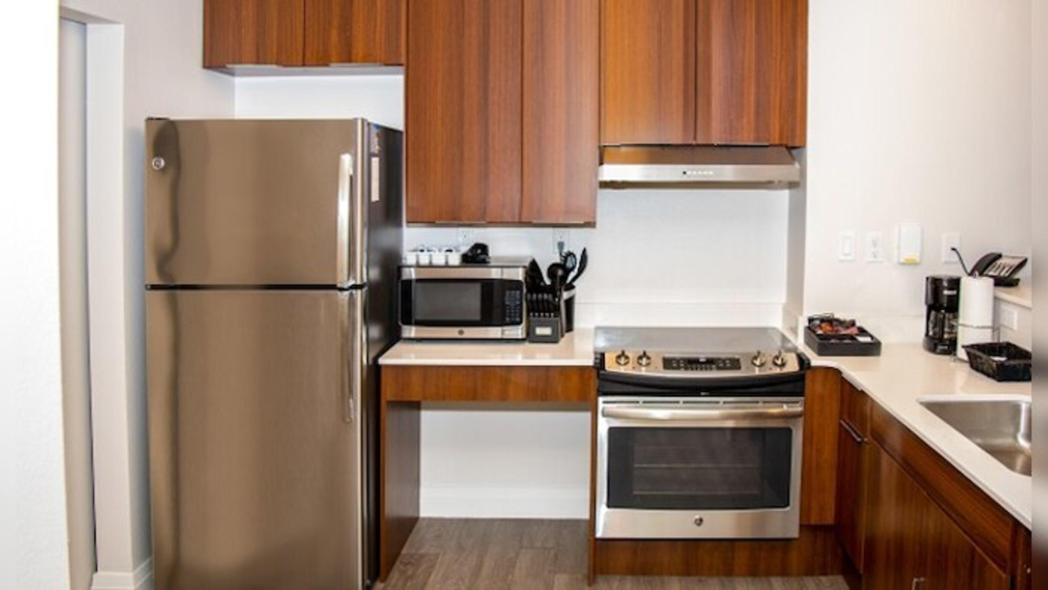 Eine kompakte Küche mit Edelstahl-Kühlschrank, Mikrowelle, Backofen und Holzschränken.